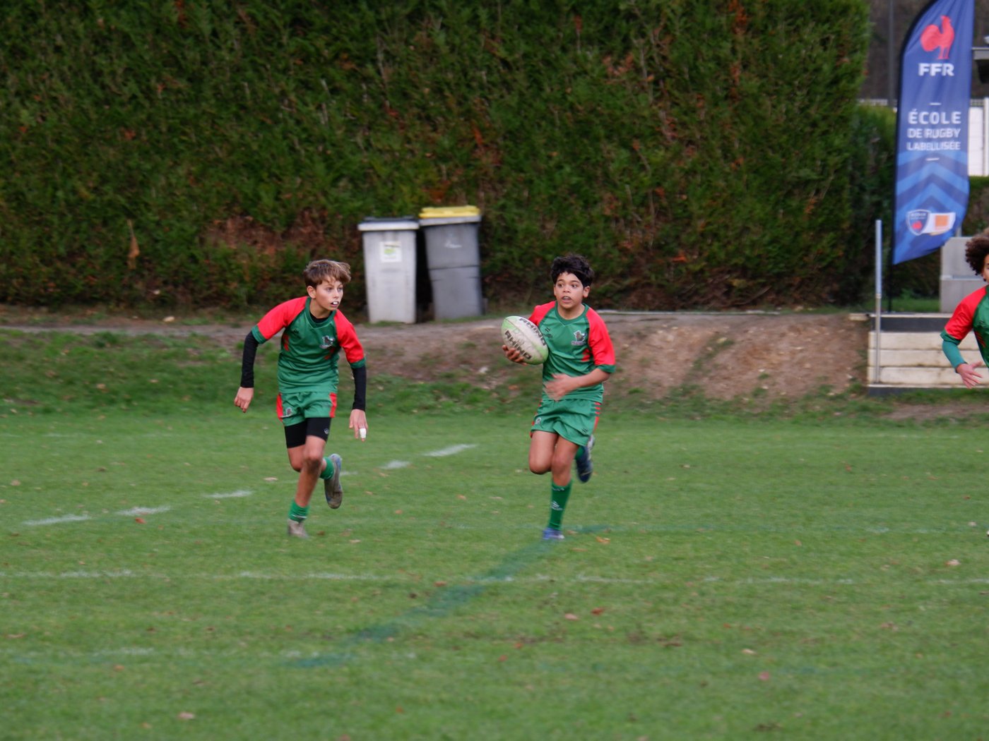 Joueurs U14 en course, balle en main, devant le fanion École de rugby labellisée FFR